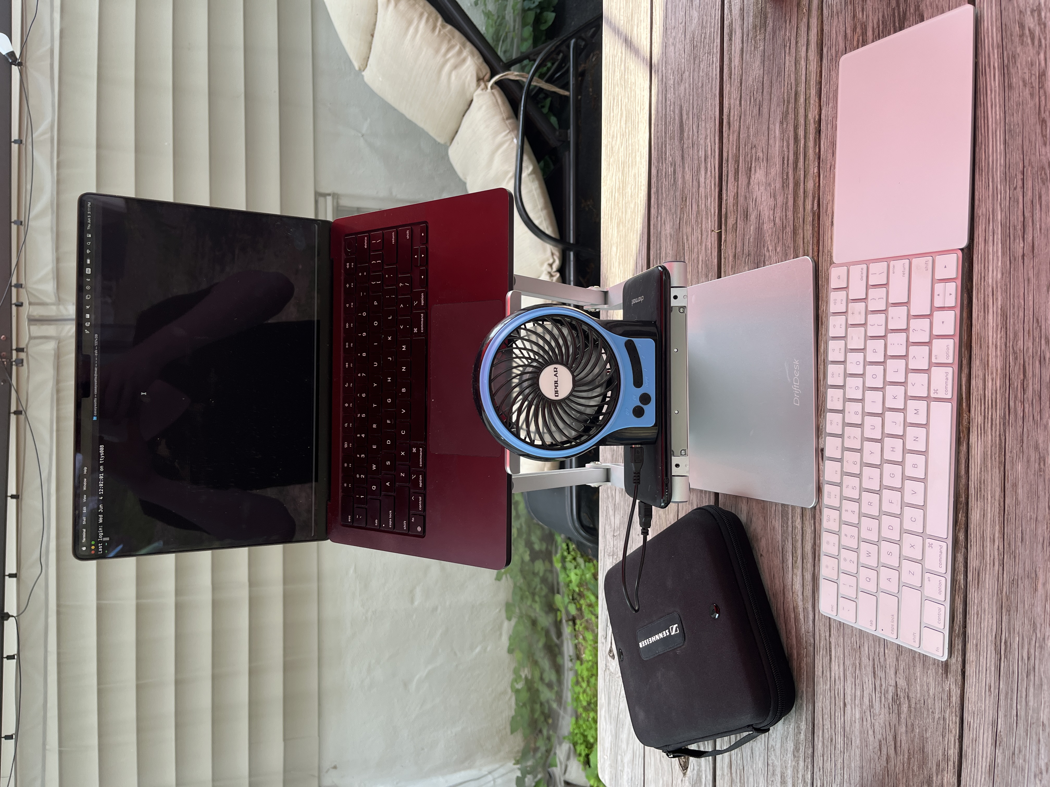 Casey's laptop setup outdoors: laptop on a stand, wireless trackpad and keyboard, headset, portable fan, portable battery pack - all on a picnic table